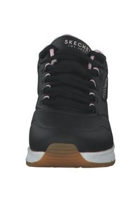 Zapatilla deportiva negra con una parte superior sintética suave, acentos en rosa, cordones redondos, cuello acolchado y una suela de goma texturizada.