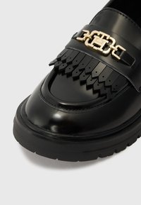 Sorte lær loafer med en blank finish, med en dekorativ gullkjededetalj og frynsepryd på vampen. Gummisåle.