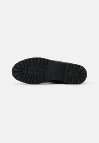 Suela de zapato de goma negra con profundos surcos y patrones cruzados para tracción. Superficie lisa alrededor de los lados, diseñada para la durabilidad.