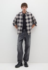 Camisa a cuadros en gris y negro; camiseta negra lisa debajo. Jeans grises holgados con costuras en contraste y zapatos negros.