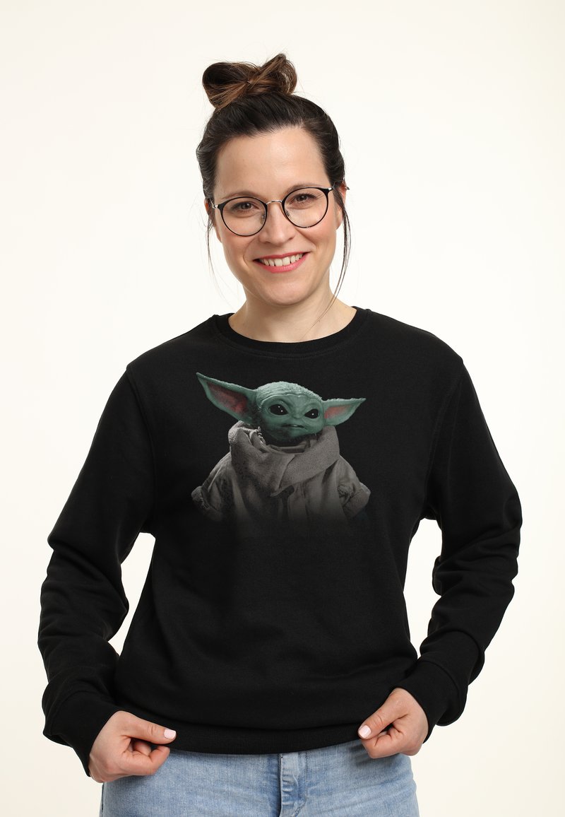 Sort sweatshirt med grafik af en grøn hudfarvet karakter med store ører og øjne, iført en grå kappe. Casual pasform med ribbede manchetter.