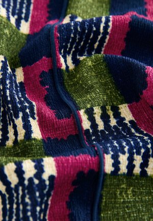 Texturiertes Gewebe in lebhaften Farben wie Grün, Marineblau, Pink und Creme mit einem gemusterten Design, das kräftige Streifen und Formen zeigt. Sichtbare Nahtdetails.