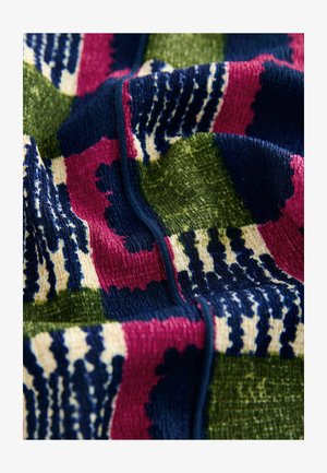 Textured fabric in vibrant colors of green, navy, pink, and cream with a patterned design featuring bold stripes and shapes. Visible seam detail.