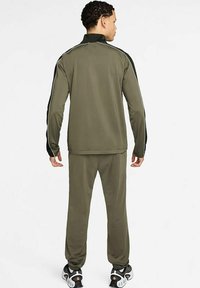 Chándal verde olivo con chaqueta con cremallera y pantalones elásticos; presenta detalles negros a lo largo de las mangas y una textura suave.