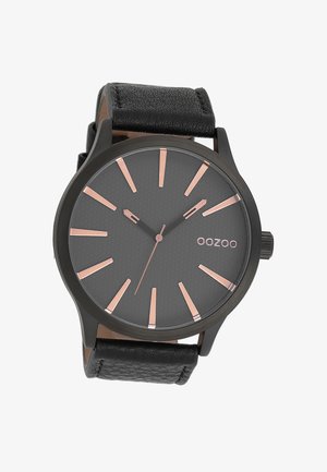 Montre analogique noire avec un cadran gris texturé, des index d'heure en or rose, et un bracelet en cuir noir. Présente un boîtier rond et un design minimaliste.