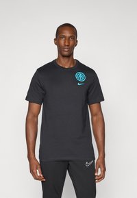 Sort bomulds t-shirt med rund halsudskæring. Har et blåt cirkulært logo og en blå Nike swoosh på brystet. Korte ærmer, standart pasform.