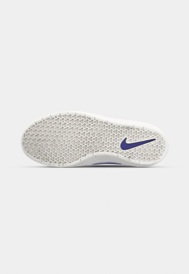 Die Sohle des Nike-Schuhs aus weißem Gummi weist ein Wabenmuster auf, mit einem lila Swoosh-Logo und einer strukturierten Oberfläche für besseren Halt.