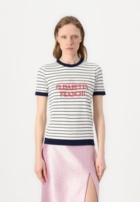 Camiseta ajustada de rayas blancas y navy con cuello redondo, que presenta un texto bordado rojo en el centro del pecho. Combinada con una falda metálica rosa.