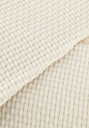 Gros plan sur un tissu de couleur crème avec un motif tricoté texturé en forme de panier, montrant des couches pliées superposées.