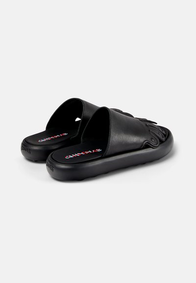 Svarta slide-sandaler i slät läder med en tjock, texturerad sula. Har en upphöjd design på övre delen och branding på innersulan.