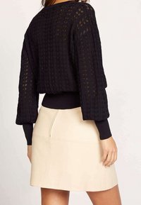 Svart stickad tröja med texturerat mönster och vida ärmar, kombinerad med en åtsittande beige läderskjol med dragkedja baktill.