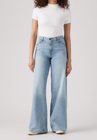 Höga, ljusblå vida jeans i denim. Har en klassisk femficksdesign och subtila blekningar på benen.