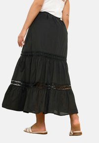 Falda larga negra con volantes y detalles de encaje, elaborada en una tela ligera. Presenta una cinturilla elástica y una forma acampanada con una textura suave.