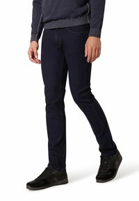 Donkerblauwe denim jeans met een slim fit, voorzien van subtiele stiksels en een vijf-pocket ontwerp. Gecombineerd met zwarte sportschoenen.