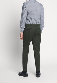 Pantalon vert sur mesure avec une texture lisse, coupe slim et poches arrière. Associé à une chemise à manches longues à motifs dans des couleurs claires.