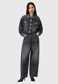 Geknipte zwarte spijkerjack met bloemknopen, gecombineerd met hoog-waist, wijde zwarte spijkerbroek. Soepele textuur, casual fit.