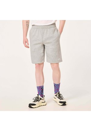 Graue Sportshorts mit elastischem Bund und Seitentaschen, kombiniert mit lila und blauen gemusterten Socken sowie schwarz-weißen Sneakern.