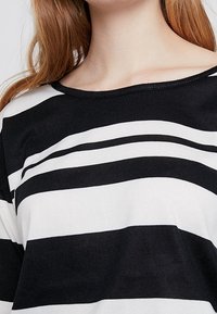 Schwarz-weißer gestreifter Oberteil mit weitem Rundhalsausschnitt und weichem, strukturiertem Stoff. Verfügt über kräftige horizontale Streifen in unterschiedlicher Breite.
