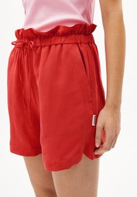 Shorts en lin rouges avec une taille élastique froncée, des poches latérales et une petite étiquette sur l'ourlet. Texture douce et design léger.