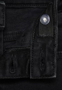 Lähellä mustaa denimmikuitua, jossa on nappikiinnitys, ommeltuja yksityiskohtia ja vyölenkkejä, sekä sileä pinta.
