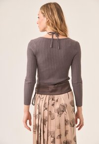 Top gris de manga larga con canalé y detalle de lazo en la parte posterior, combinado con una falda plisada con estampado floral en colores suaves y una cinturilla de satén.
