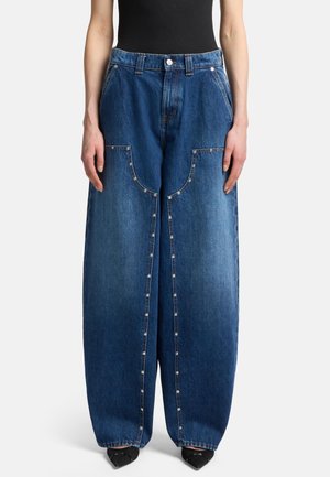 Blue denim wide-leg jeans featuring unique enlarged pockets, silver snap buttons on the front seam, and a faded texture.