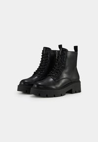 Bottines en cuir noir avec une semelle épaisse, présentant un laçage à l'avant et une fermeture éclair sur le côté. Texture lisse avec des détails de couture et une languette de tirage.