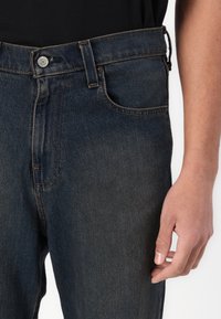 Dark blue denim jeans featuring a classic design, five pockets, a button closure, and subtle stitching details on the seams.