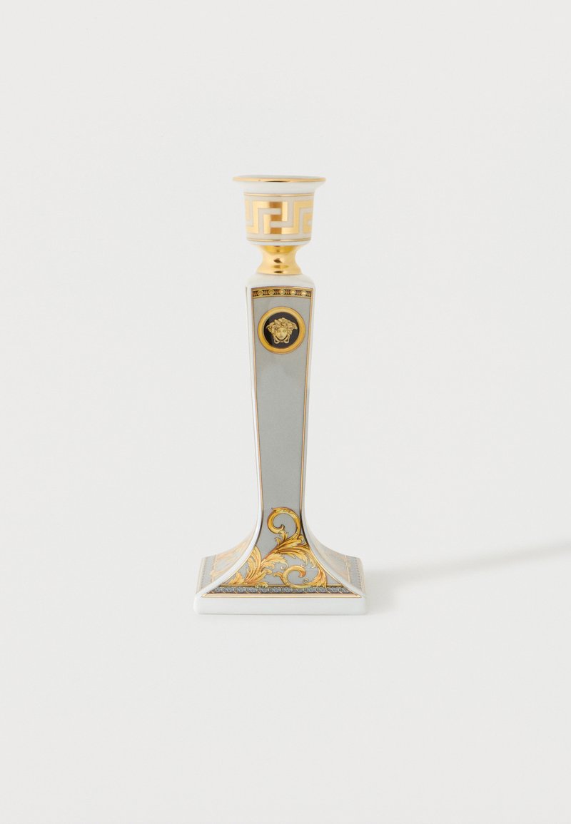 Valkoinen ja kullanvärinen koristeellinen kynttilänjalka nelikulmaisella jalustalla, koristeellisilla kullanvärisillä lehtikuviolla ja Medusan tunnuksella varressa.