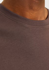Kortærmet brun bomulds t-shirt med ribbet rund hals, der har en glat tekstur og en tætsiddende form. Ingen grafik eller udsmykninger.