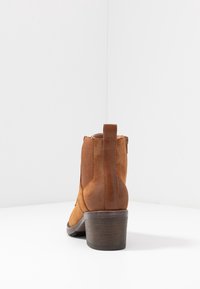 Bottines brunes en suède lisse, avec un talon en bois effilé, des panneaux latéraux élastiques et un détail cousu à l'arrière.