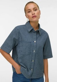 Camisa de manga corta, con cuello, en azul marino con rayas blancas. Cuenta con un bolsillo frontal y botones plateados, confeccionada en una tela texturizada.