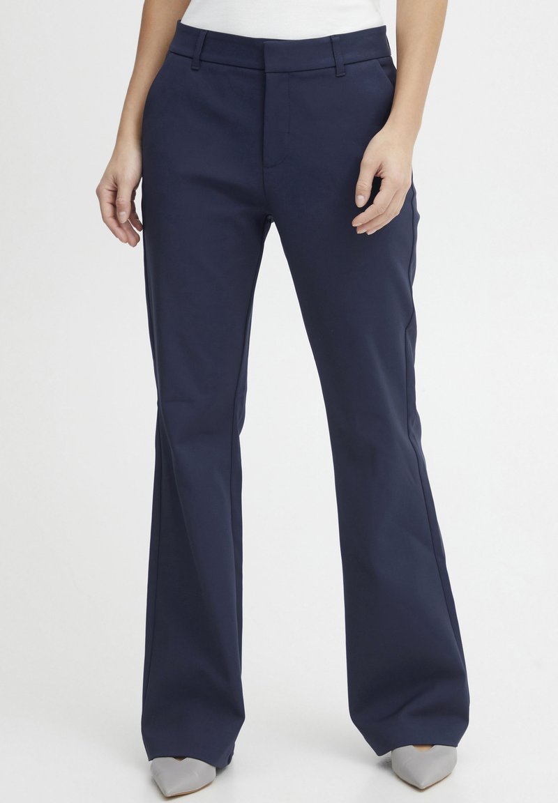 Navy blue flared trousers made of smooth fabric, featuring a flat front, side pockets, and a tailored fit, paired with pointed gray shoes.