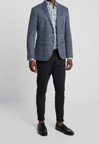 Herrarnas skräddarsydda marinblå kavaj i texturerad tyg, tillsammans med en blommönstrad skjorta, svarta slim fit-byxor och svarta loafers.
