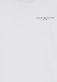 Hvit bomull T-skjorte med rund hals, med en liten svart logo "TOMMY HILFIGER EST. 1985" på venstre brystområde. Glatt tekstur.