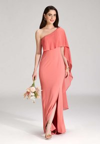 Ein ärmelloses Kleid in Korallenfarbe mit geschichteter Stoffdrape, figurbetontem Design, seitlichem Schlitz und leichter Textur. Das Model hält einen Blumenstrauß.