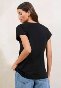 T-shirt nero a maniche corte, materiale in cotone leggero, scollatura rotonda, vestibilità morbida, indossato con jeans di denim blu chiaro, texture liscia.