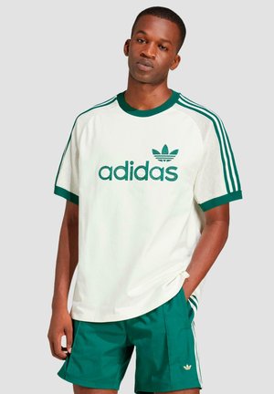 Bílá krátká tričko s krátkým rukávem a zelenými akcenty, obsahující síťované panely, vyšívané logo "adidas" a zelené šortky s logem na lemu.