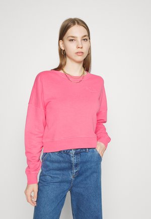 Lyserød cropped sweatshirt med rund halsudskæring, ribbede manchetter og broderet logo. Parret med højtaljede blå denim jeans.