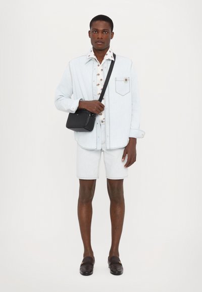 Camicia di jeans azzurro chiaro con taschino, camicia floreale sotto, pantaloni corti di jeans chiaro, borsa a tracolla nera e scarpe scivolate scure.