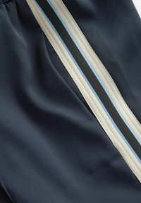 Shorts marine en tissu lisse, avec un motif rayé vertical beige, noir et bleu clair sur un côté.
