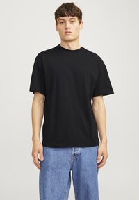 Czarna bawełniana koszulka z okrągłym dekoltem, krótkimi rękawami, luźnym krojem i gładką fakturą, w połączeniu z jasnoniebieskimi dżinsami.