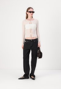 Hvit gjennomsiktig langermet topp med snøring, kombinert med høy midje svarte jeans. Tilbehør inkluderer mørke solbriller og en liten håndveske.