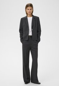 Sötétszürke, szabott blézer egy gombos záródással, hozzá illő, széles nadrágokkal és alatta egy fehér pólóval.