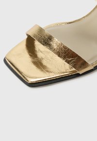Gold metallic slide sandal with a flat square toe and a single wide strap. The surface has a textured finish and a black rubber sole.