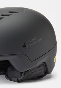 Casco de esquí negro con acabado mate, ranuras de ventilación y correas para la barbilla ajustables. Presenta un logo en relieve y una etiqueta amarilla de MIPS.