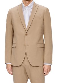 Tan jakkesæt med to knapper, notch-lapel og en enkelt brystlomme. Har en glat tekstur og matchende bukser. Hvid skjorte under.