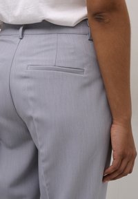 Lichtgrijze broek gemaakt van een gestructureerde stof, met een gladde tailleband en een enkele achterzak met een smalle opening.