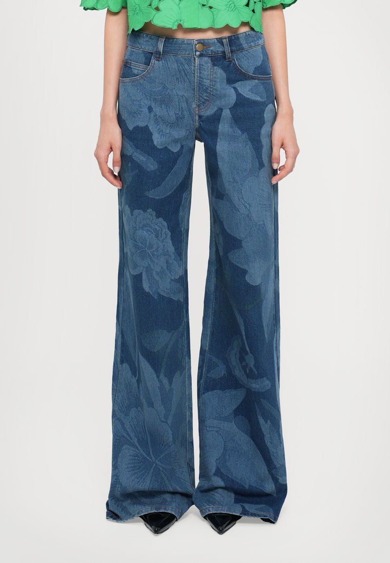 Wide-leg blue jeans with a floral pattern, featuring a high waist, subtle back pockets, and finished hems. Paired with pointed black shoes.