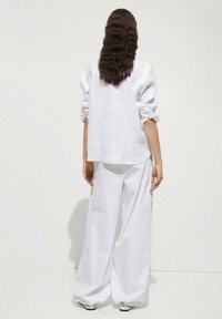 Cămașă oversized din in alb cu mâneci rulate și pantaloni albi, largi. Textură fină, design minimalist și paletă de culori neutră.